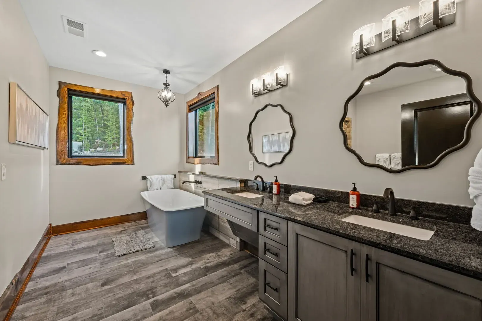 Bathroom with grey cabinets, two mirrors, and a clawfoot tub.