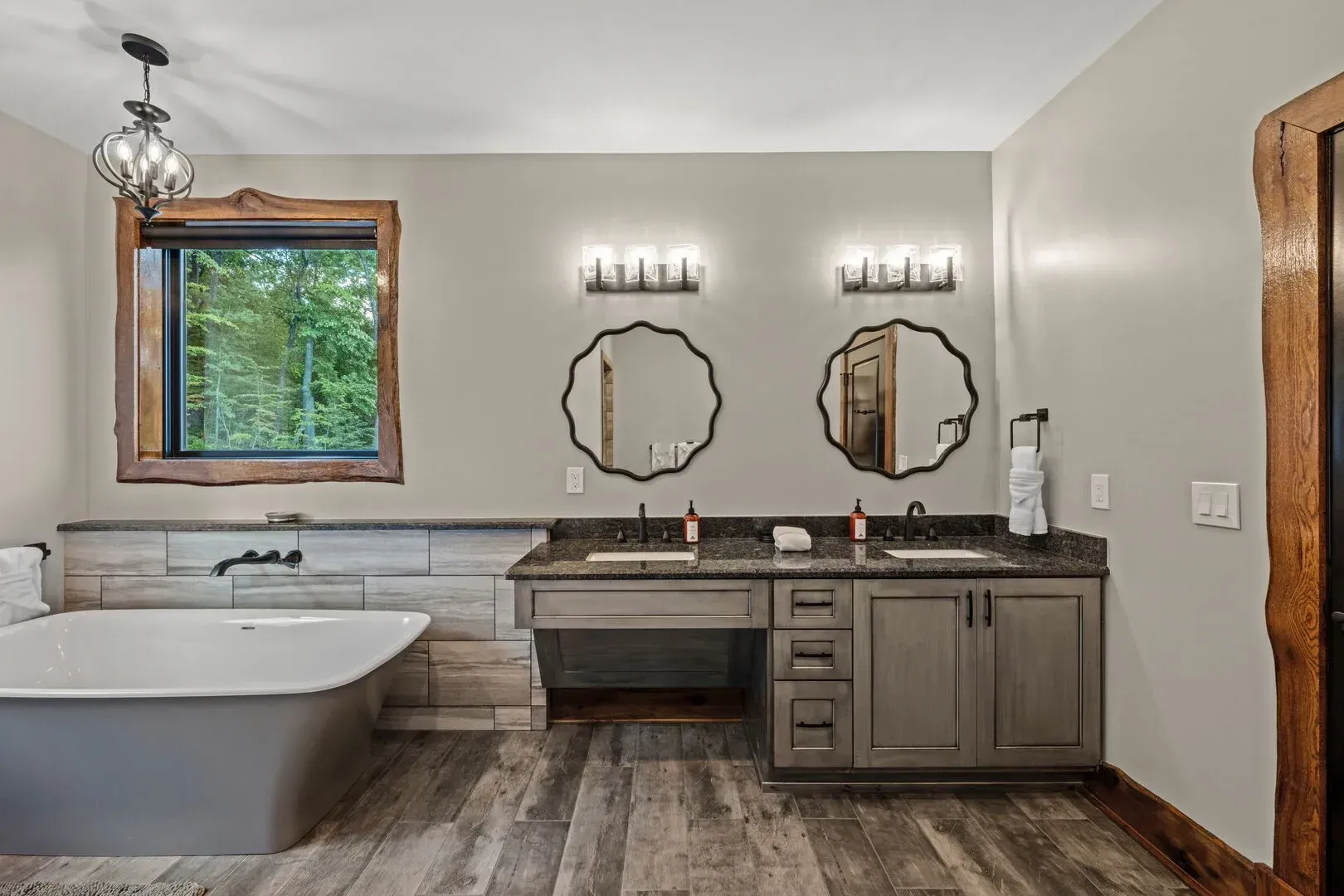 Spacious bathroom with gray cabinetry, two decorative mirrors, and a freestanding tub.