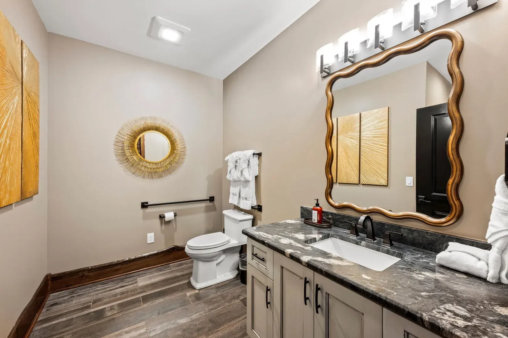 Bathroom with ornate gold mirror, gray vanity, toilet, and decorative wall art.