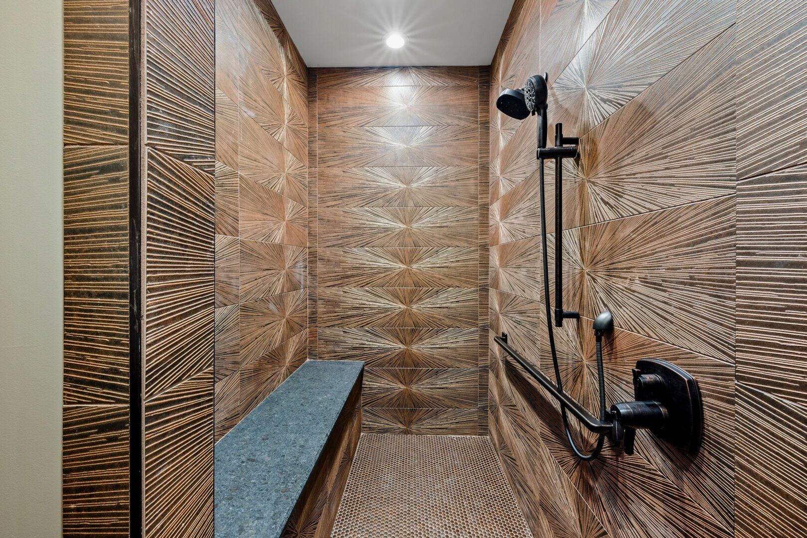 Brown-tiled shower with built-in bench, black fixtures, and patterned walls.