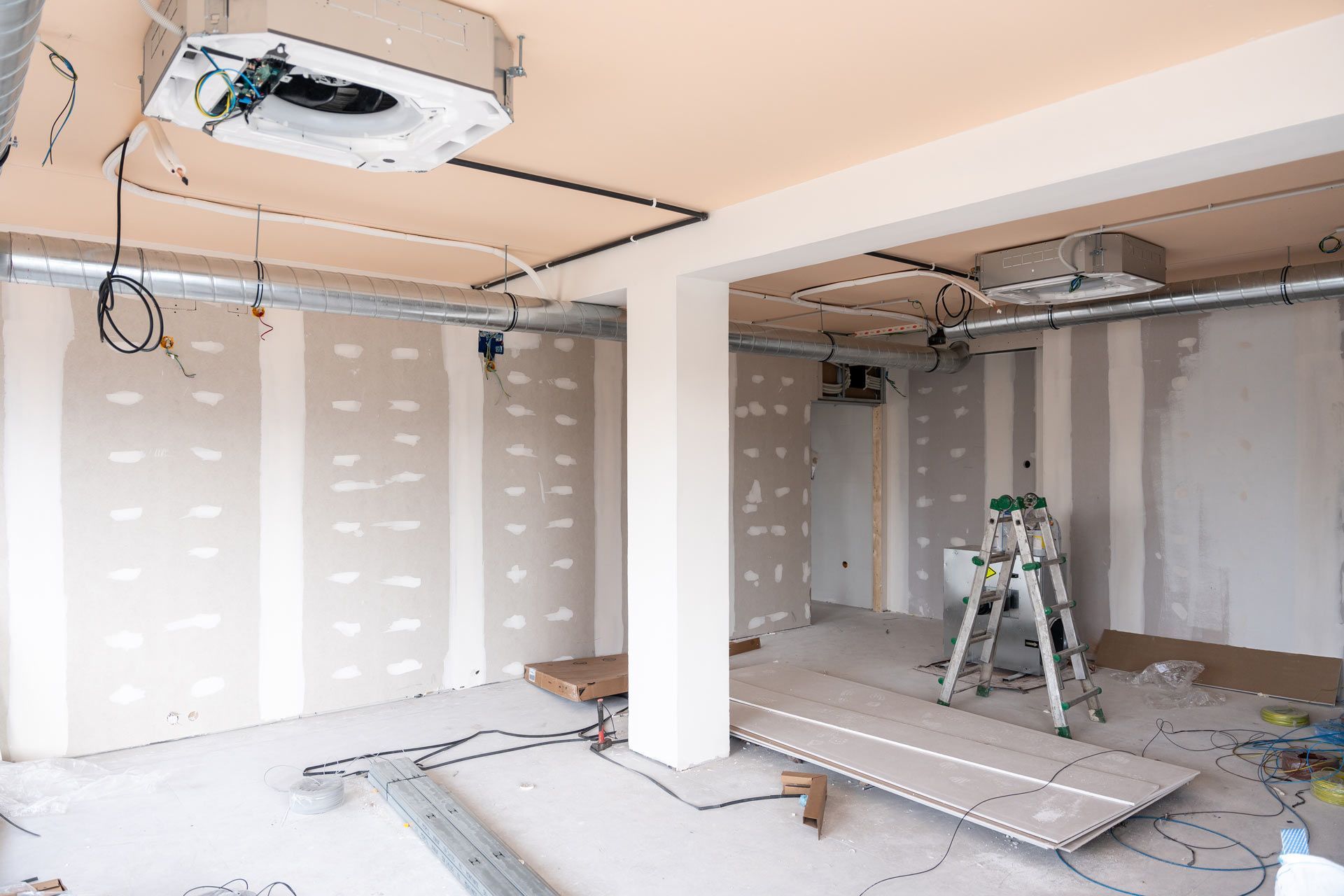 Unfinished garage interior with drywall, exposed ceiling, a ladder, and construction debris on the floor