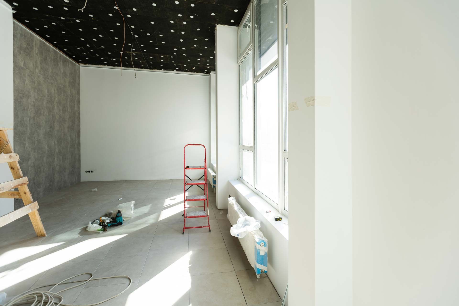 Bright unfinished room with white walls, gray floor, black starry ceiling, and a red ladder by sunlit windows