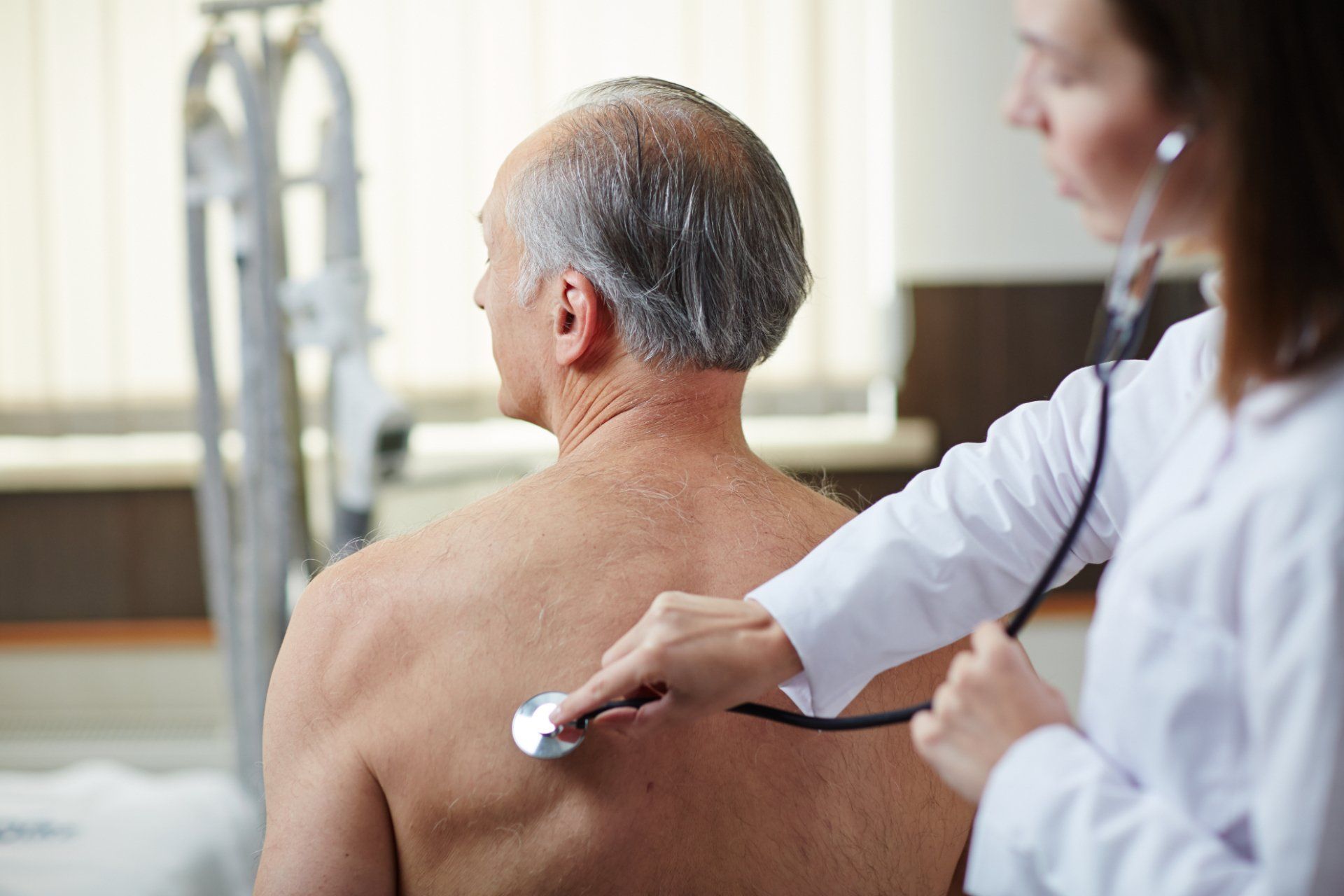 female doctor listens to elderly mans lungs