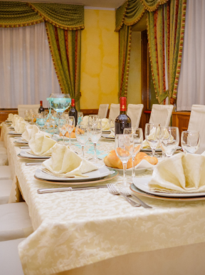 Un lungo tavolo con piatti, bicchieri, tovaglioli e una bottiglia di vino.