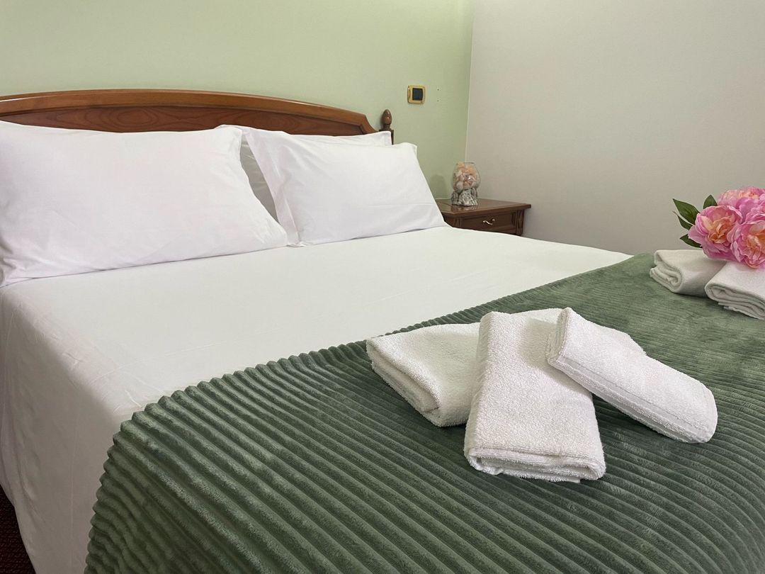 Un letto con lenzuola bianche e coperte verdi in una stanza d'albergo.