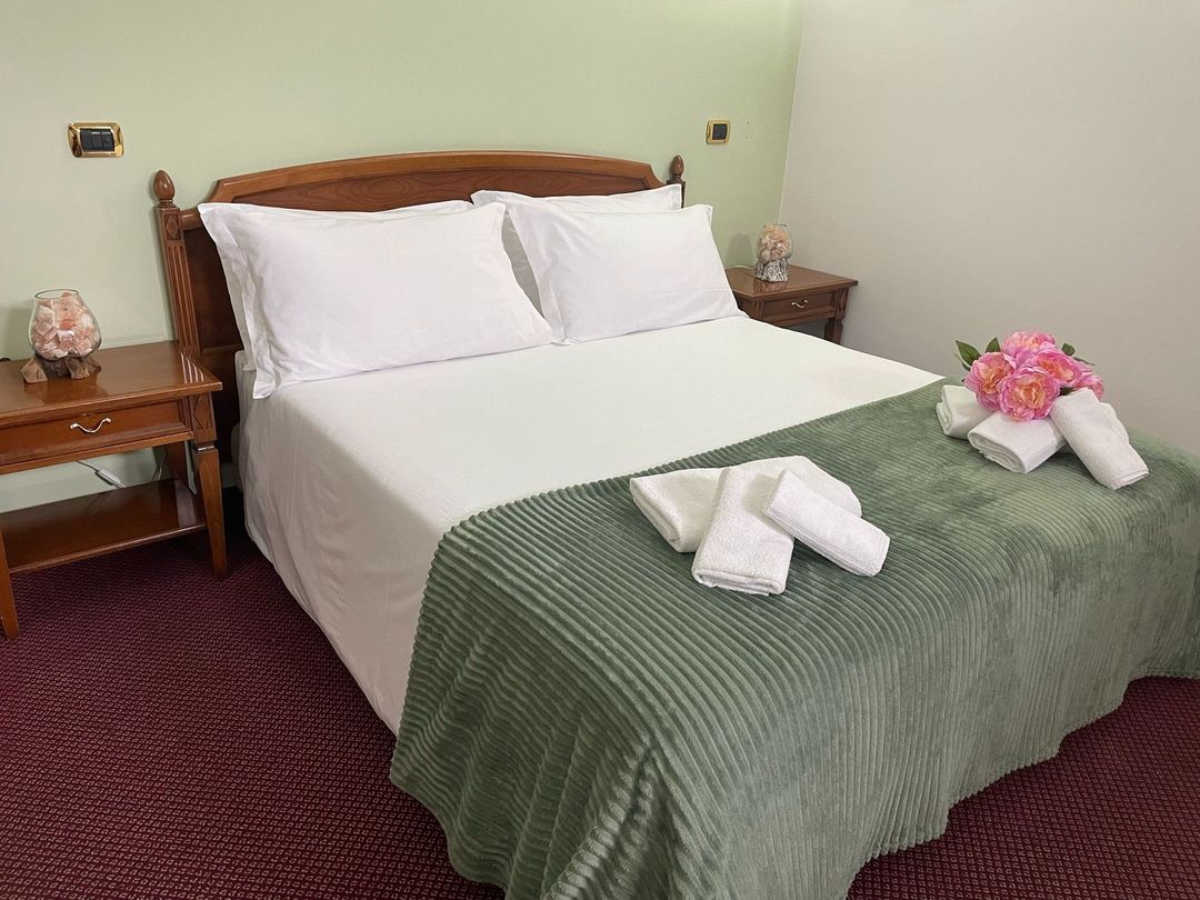 Un letto con lenzuola bianche e coperte verdi in una stanza d'albergo.