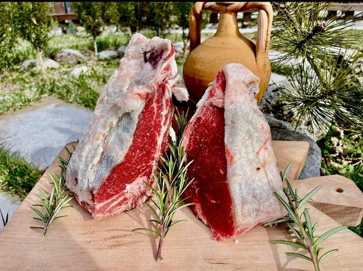 Due pezzi di carne cruda sono appoggiati su un tagliere di legno.