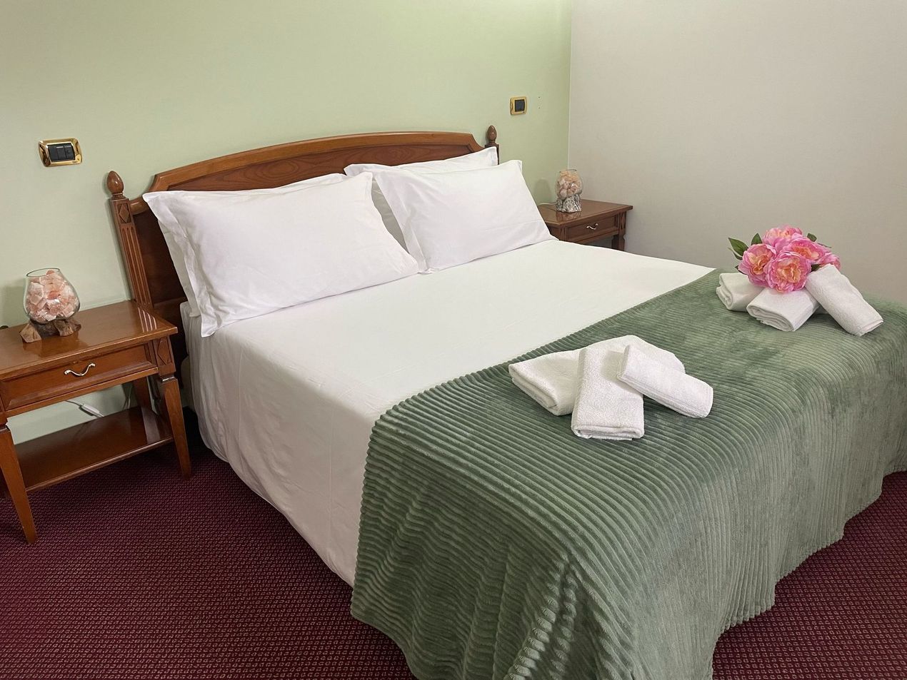 Una stanza d'albergo con un letto, due comodini e una lampada.