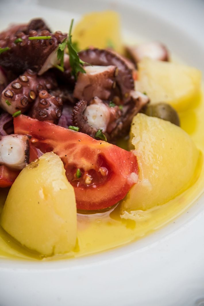 Un primo piano di un piatto di cibo con polpo, patate, pomodori e olive.