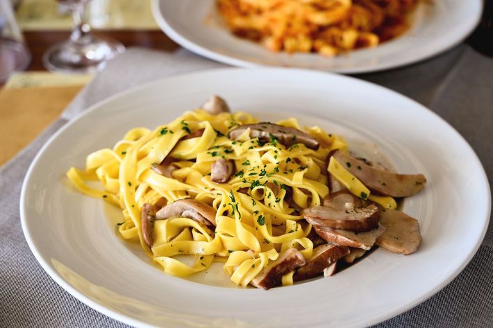 Un piatto bianco con sopra tagliatelle e funghi su un tavolo.