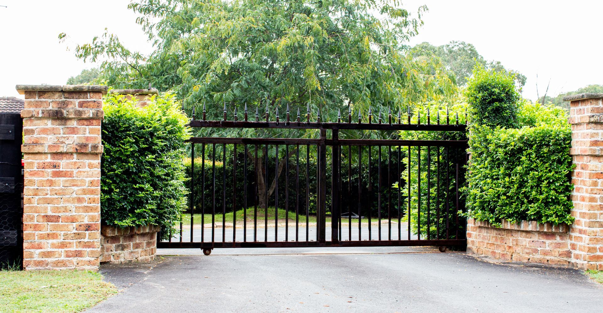 Black wrought iron gate with brick pillars and manicured hedges.