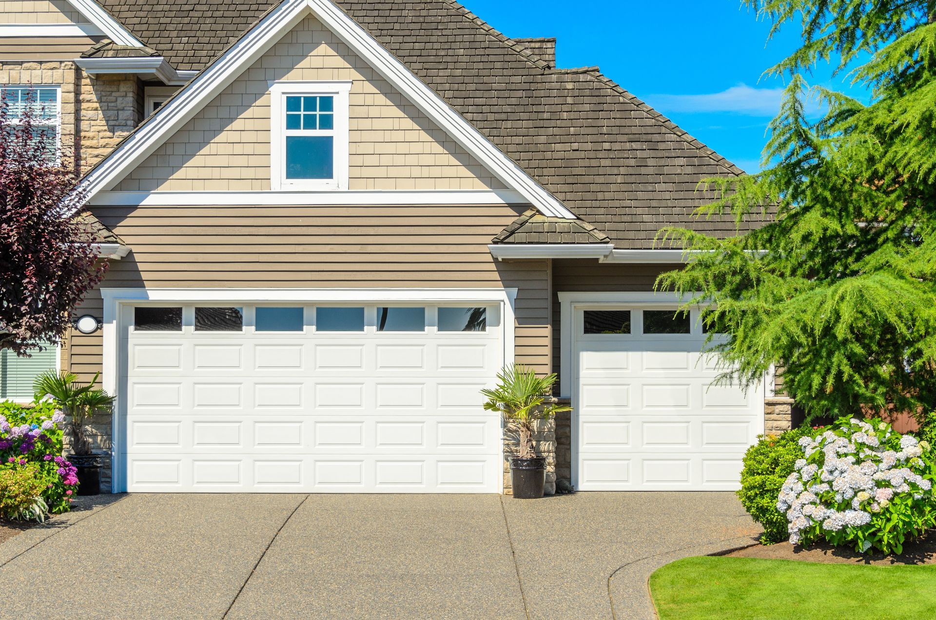Two-car garage with white doors on a house with tan siding and a brown roof.