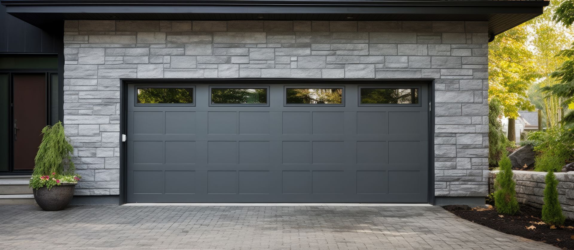 Gray garage door with stone wall exterior. Includes windows and a paved driveway.