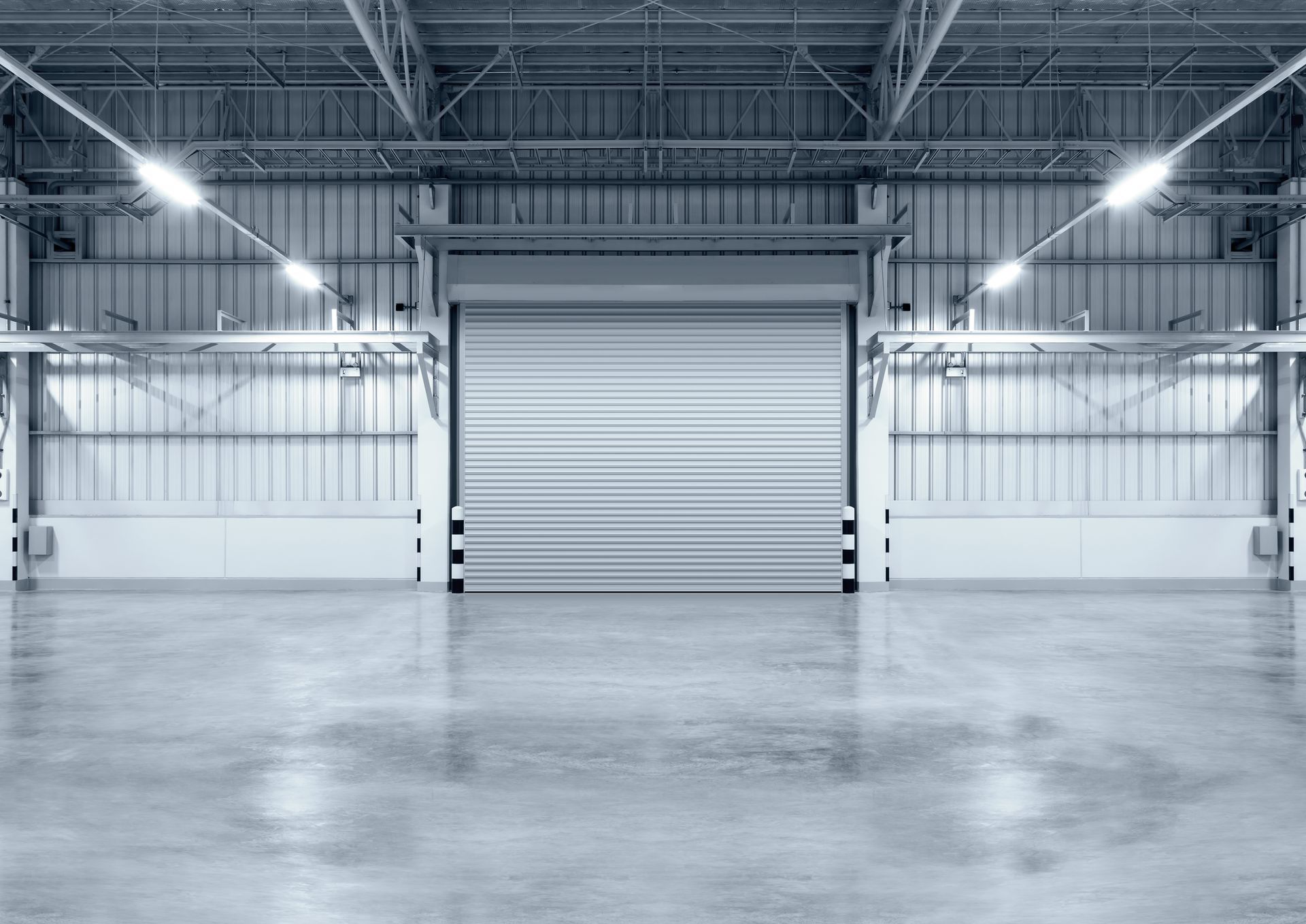 Empty warehouse interior with a closed overhead door and bright lights.