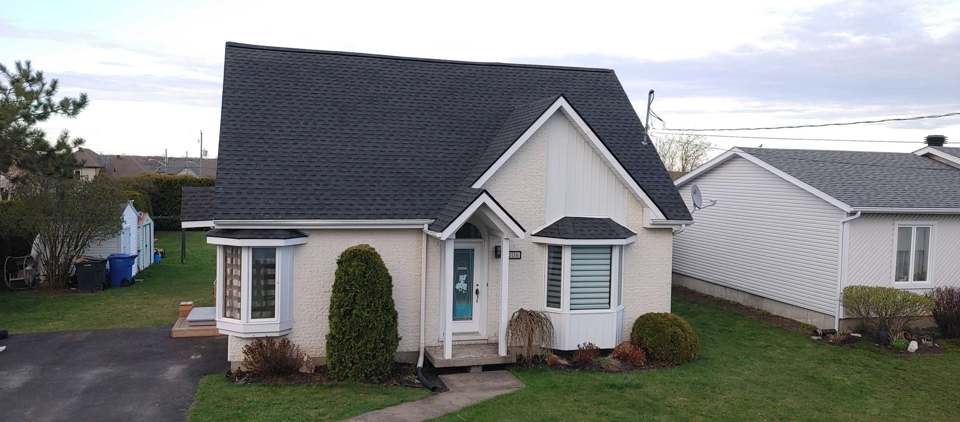 Une petite maison couleur crème, avec un toit noir et une porte d'entrée bleue, est entourée d'herbe verte.