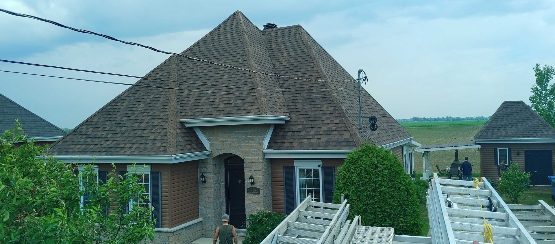 Une maison au toit complexe et à la façade en briques ; une personne s'approche de la porte.