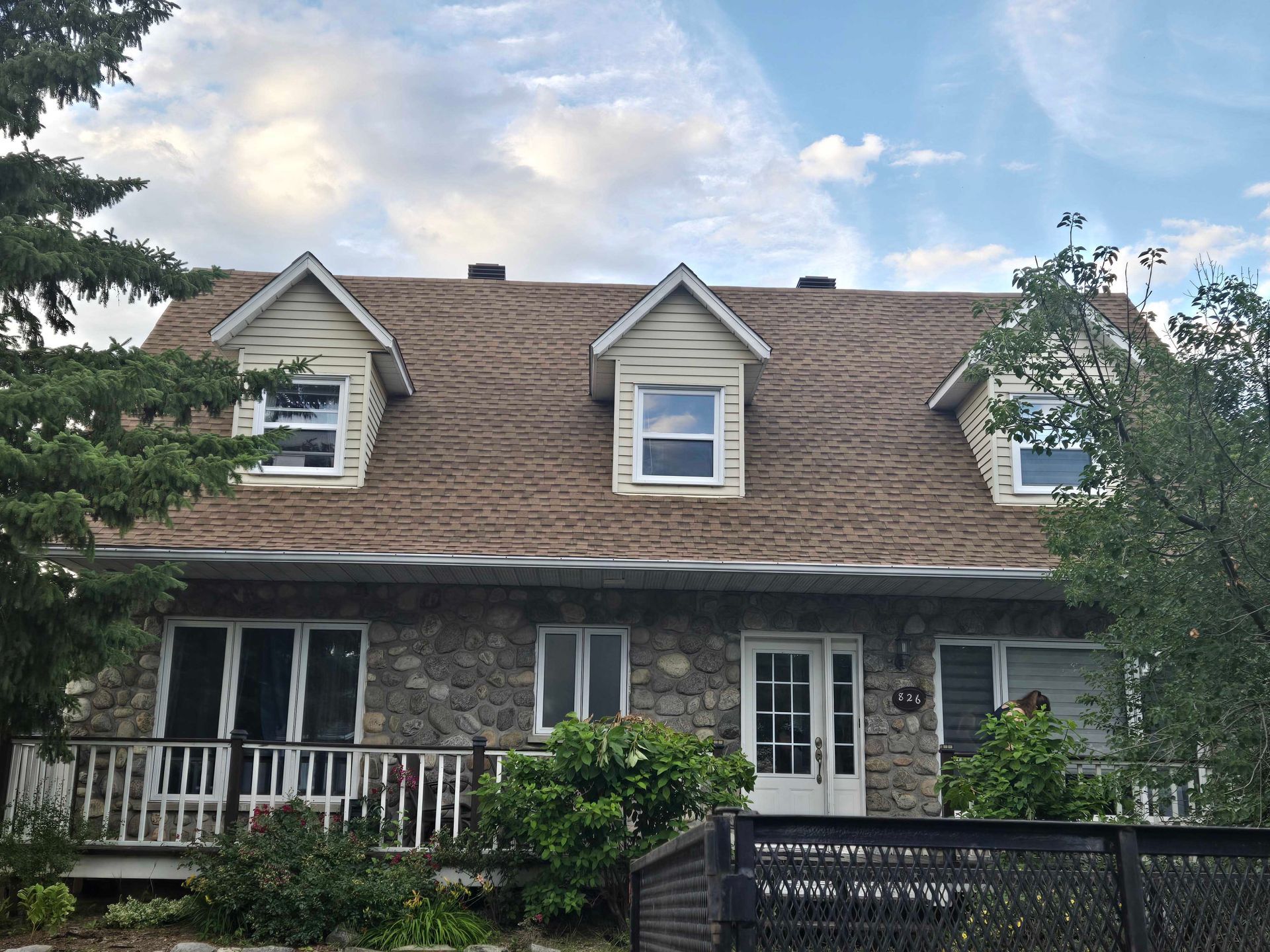 Maison en pierre avec lucarnes, porche et toit brun sur un ciel nuageux.