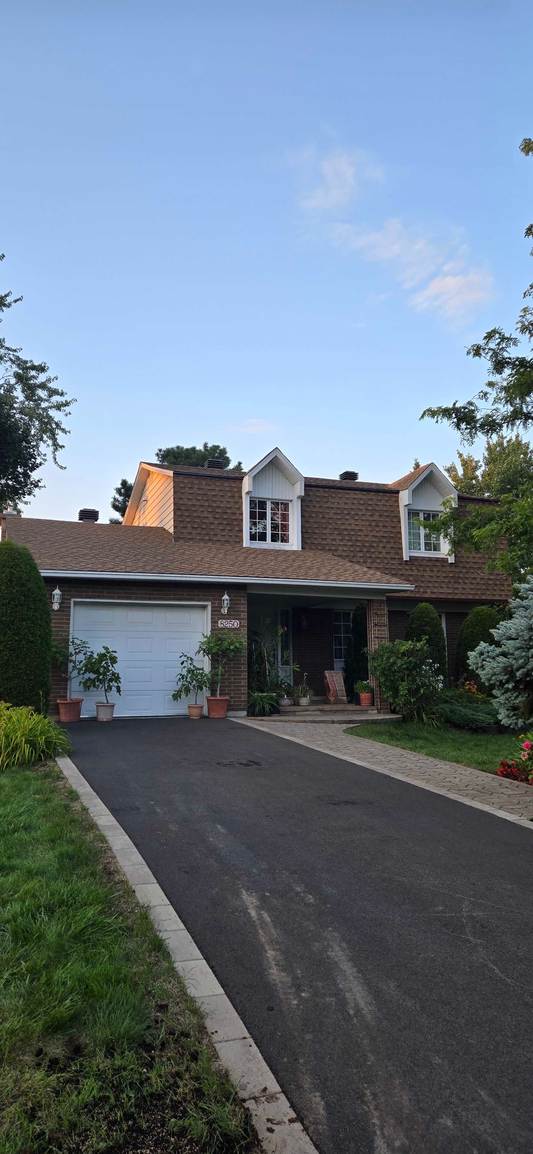 Une maison avec allée et garage, entourée de verdure sous un ciel bleu.