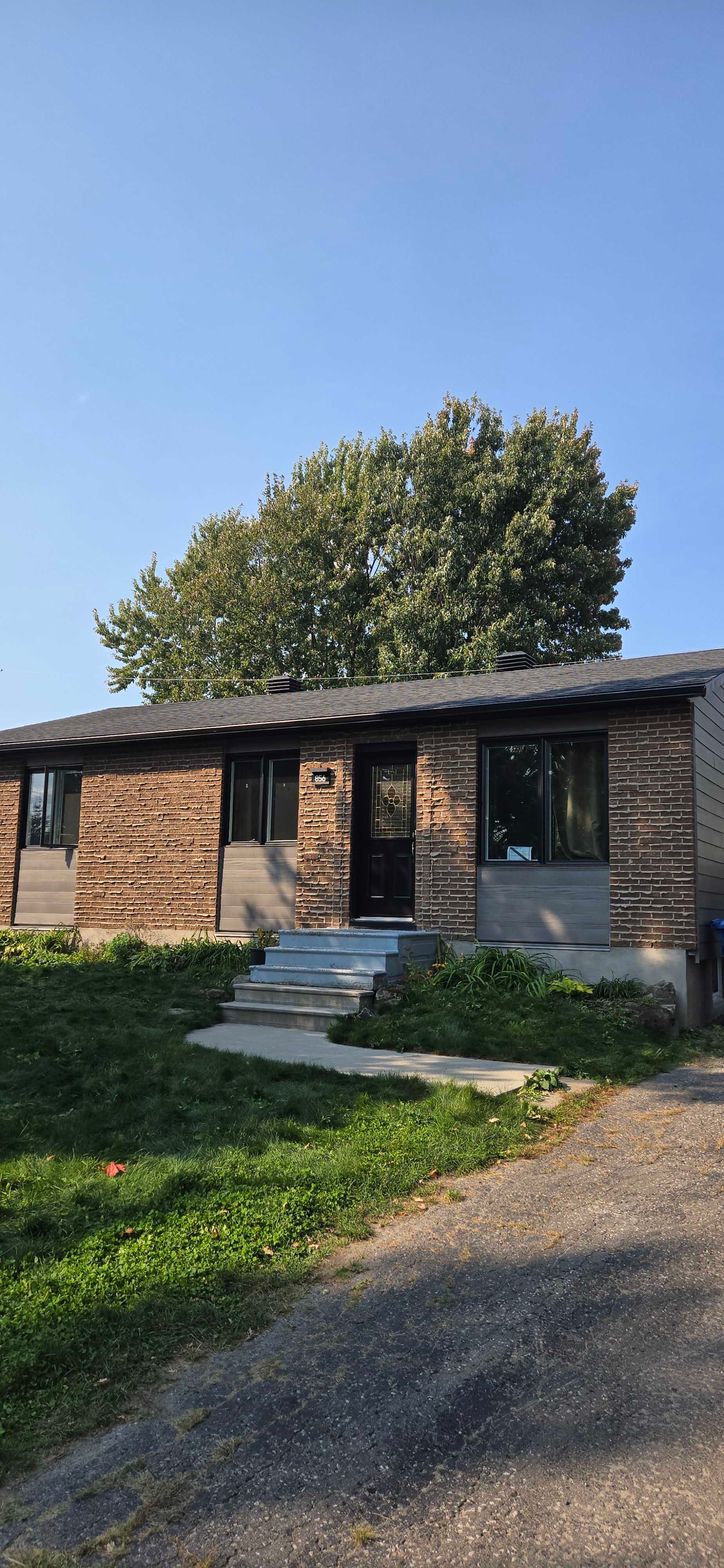 Une petite maison en briques avec une pelouse verte et un arbre en arrière-plan, sous un ciel bleu.