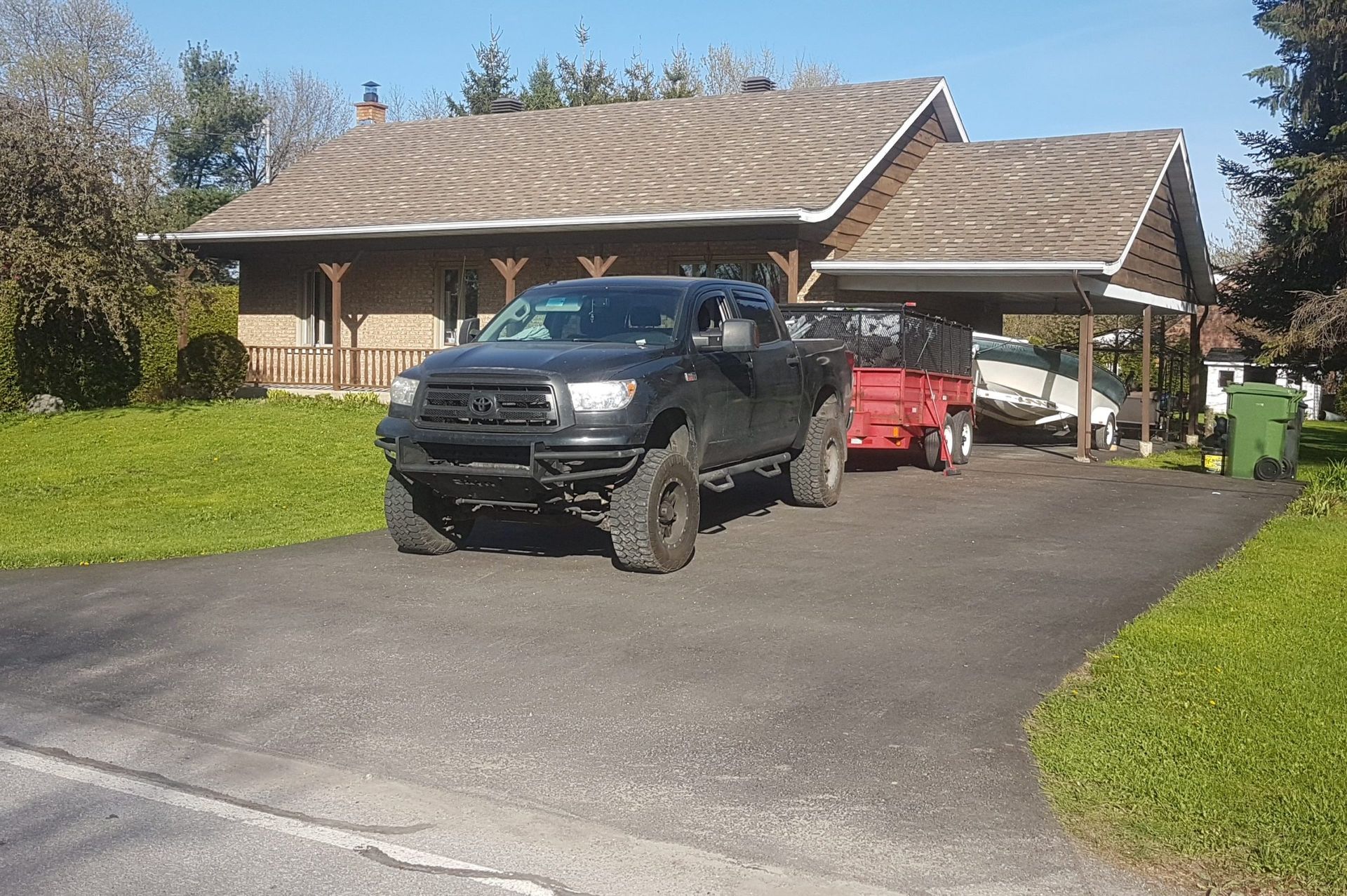 Un camion noir avec une remorque rouge est garé devant une maison au toit marron et à la pelouse verte.