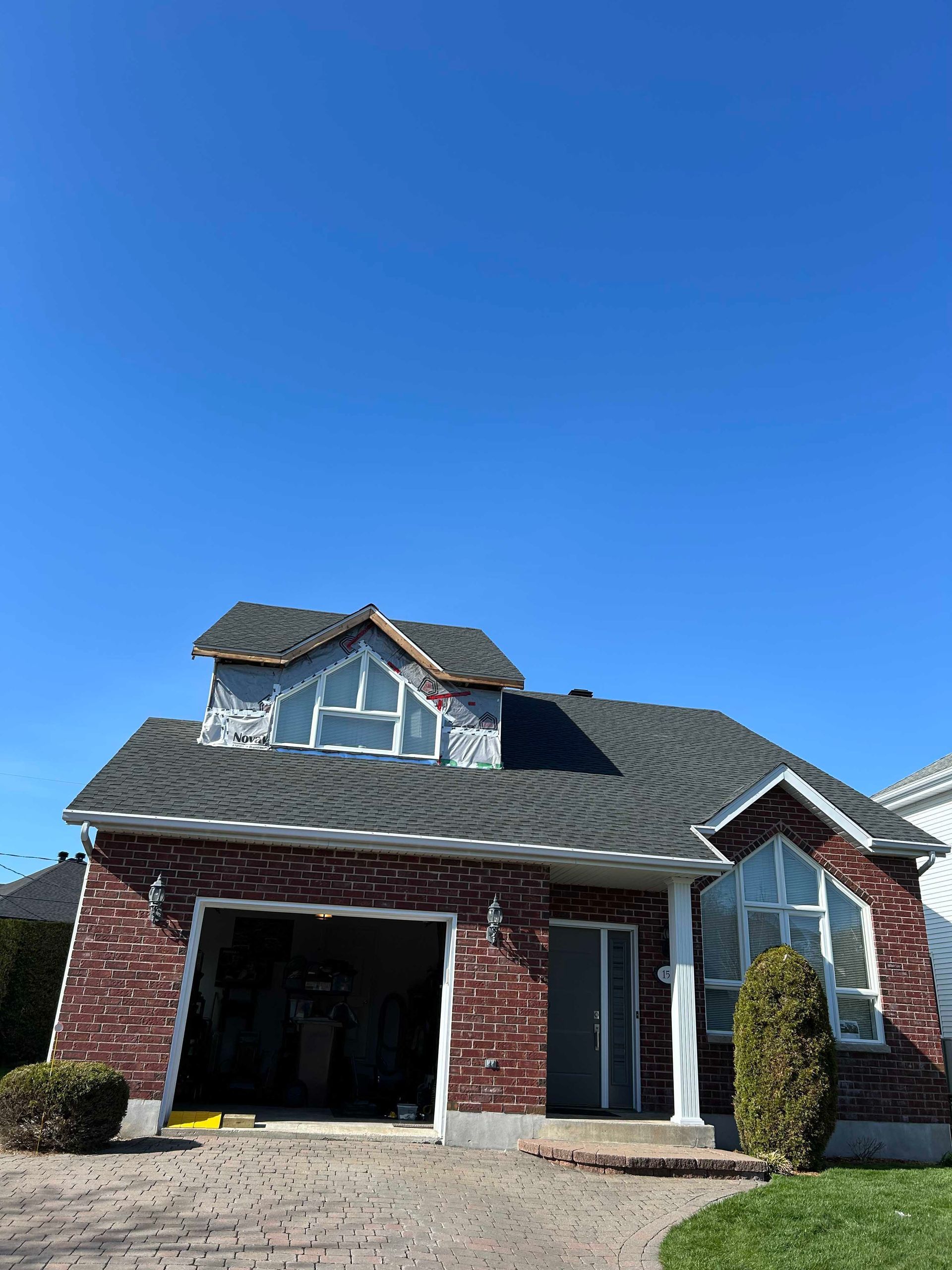 Maison en briques avec garage, fenêtres et toit sombre sous un ciel bleu.