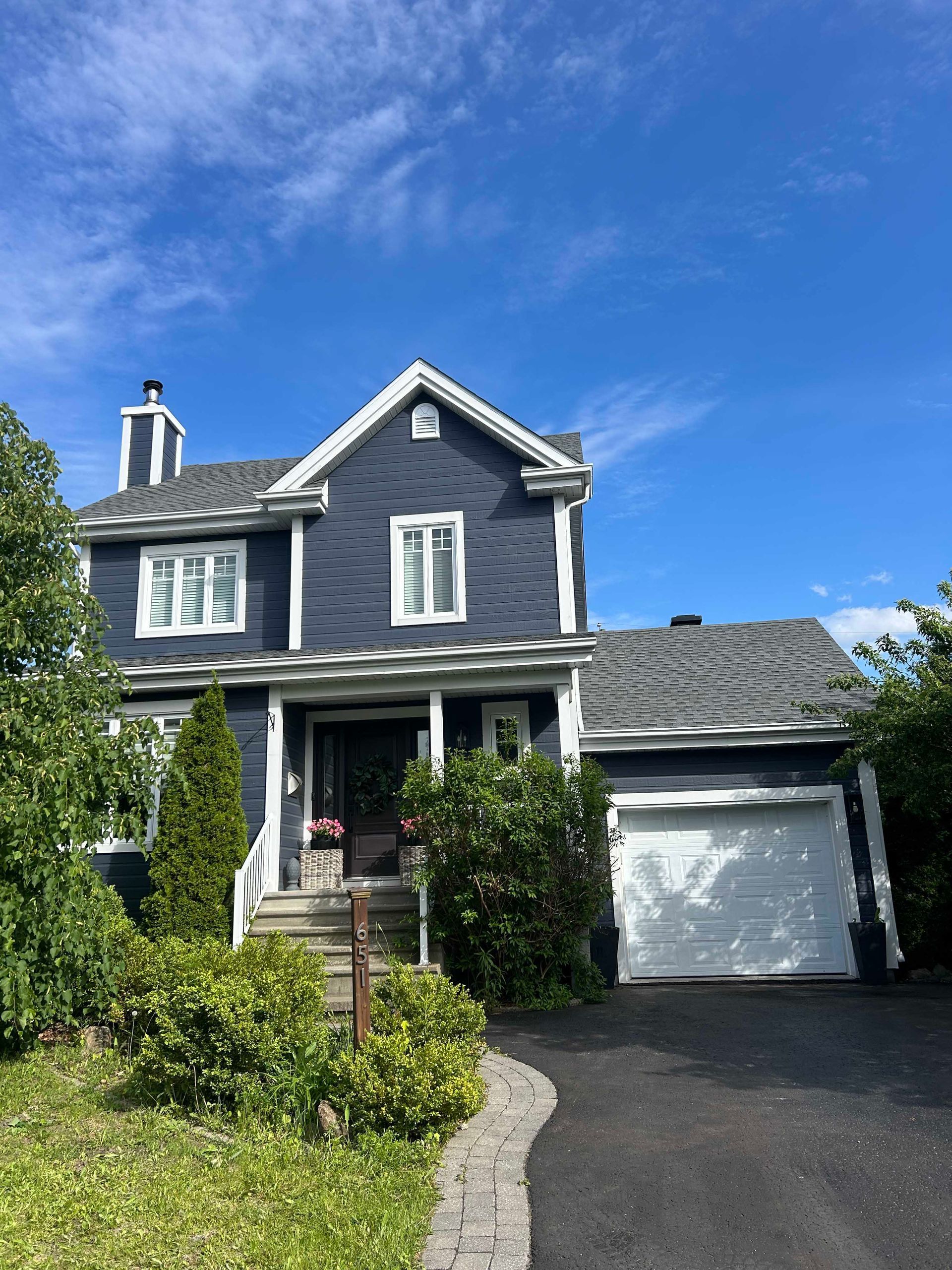 Maison bleue à deux étages avec des boiseries blanches, un toit gris et un garage attenant, sous un ciel bleu.