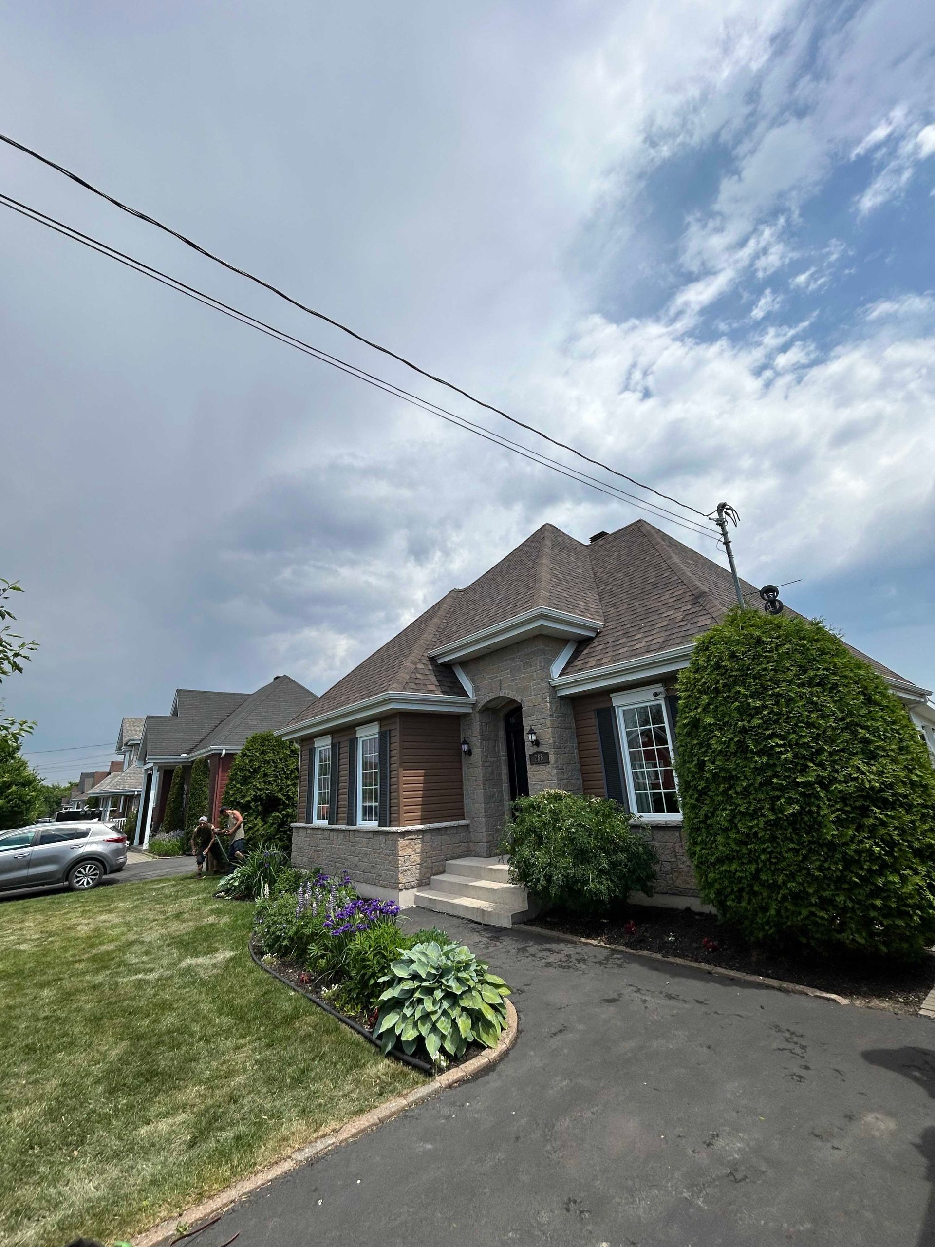 Maison en briques au toit marron, cour avant et ciel couvert.