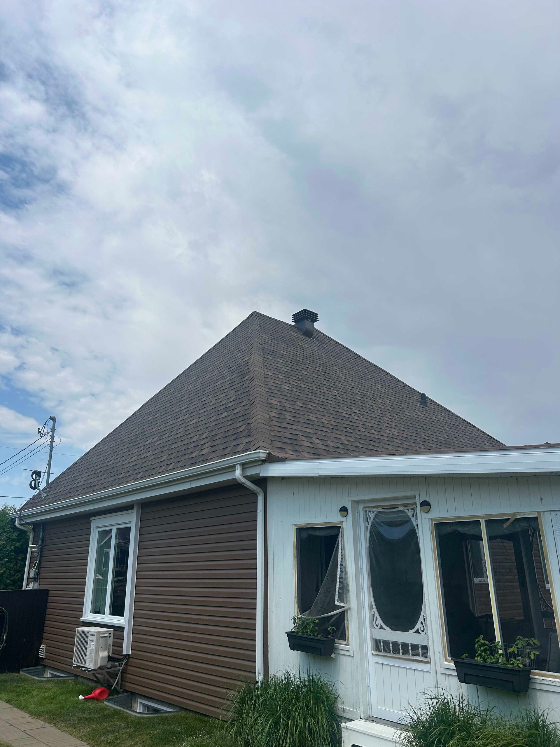 Maison au toit et aux façades marron, porche blanc, ciel bleu.