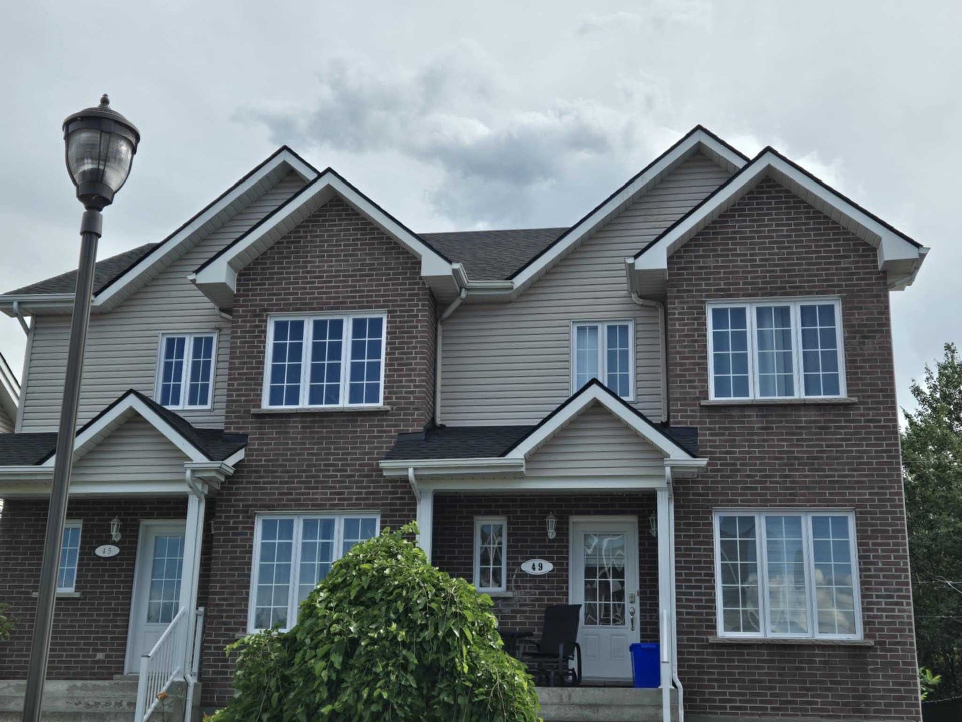 Maisons de ville en briques et bardage, sous un ciel nuageux. Portes d'entrée avec petits porches.