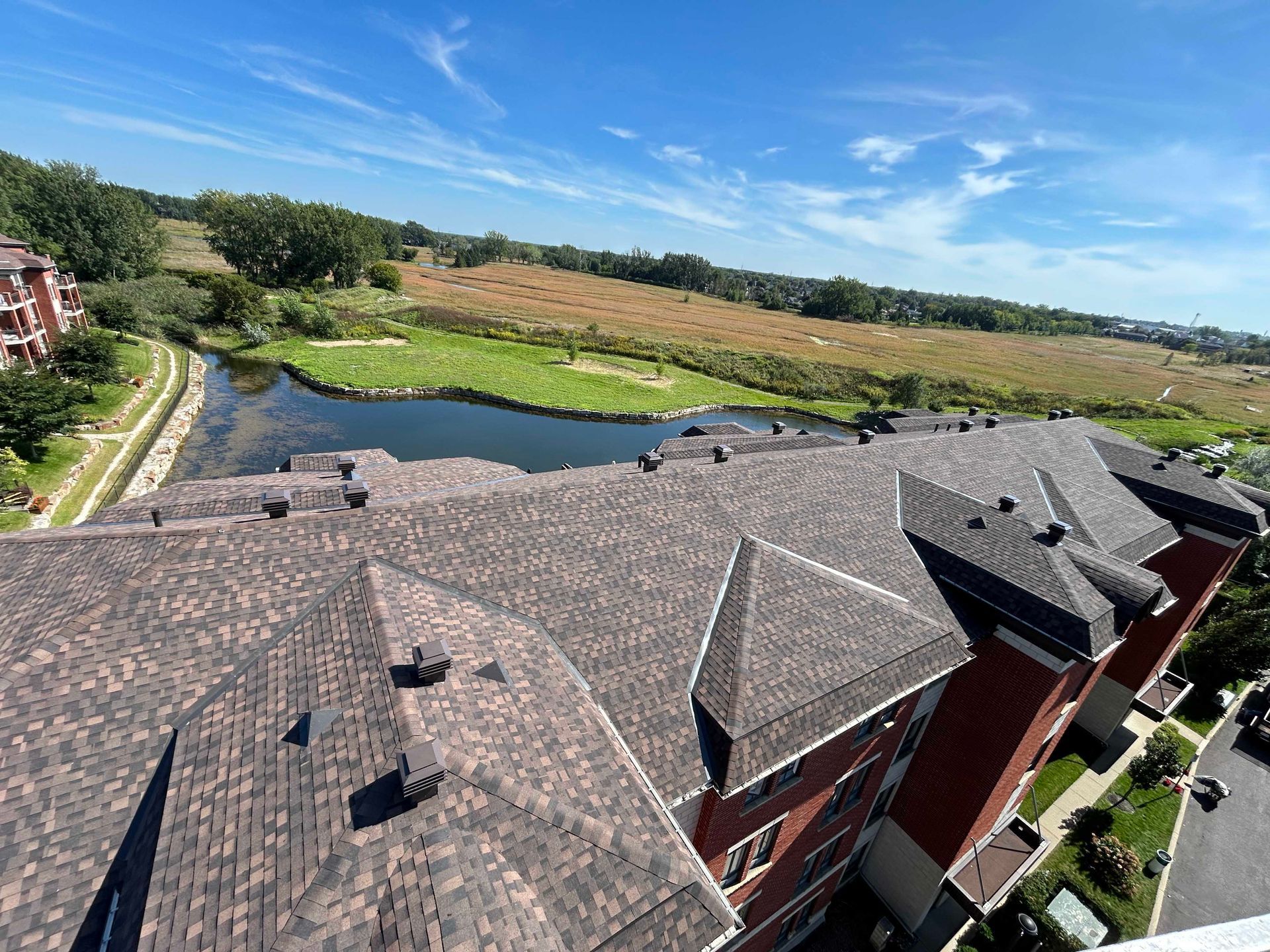 Toit brun donnant sur un étang et un champ sous un ciel bleu.