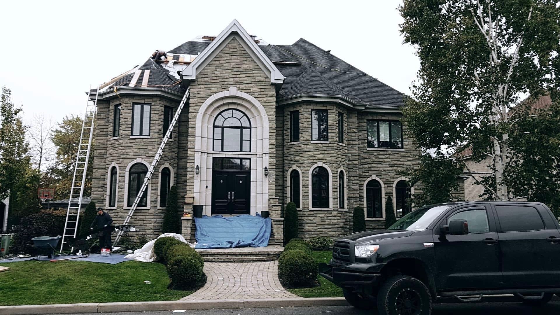 Grande maison en pierre avec toiture, camion garé devant.
