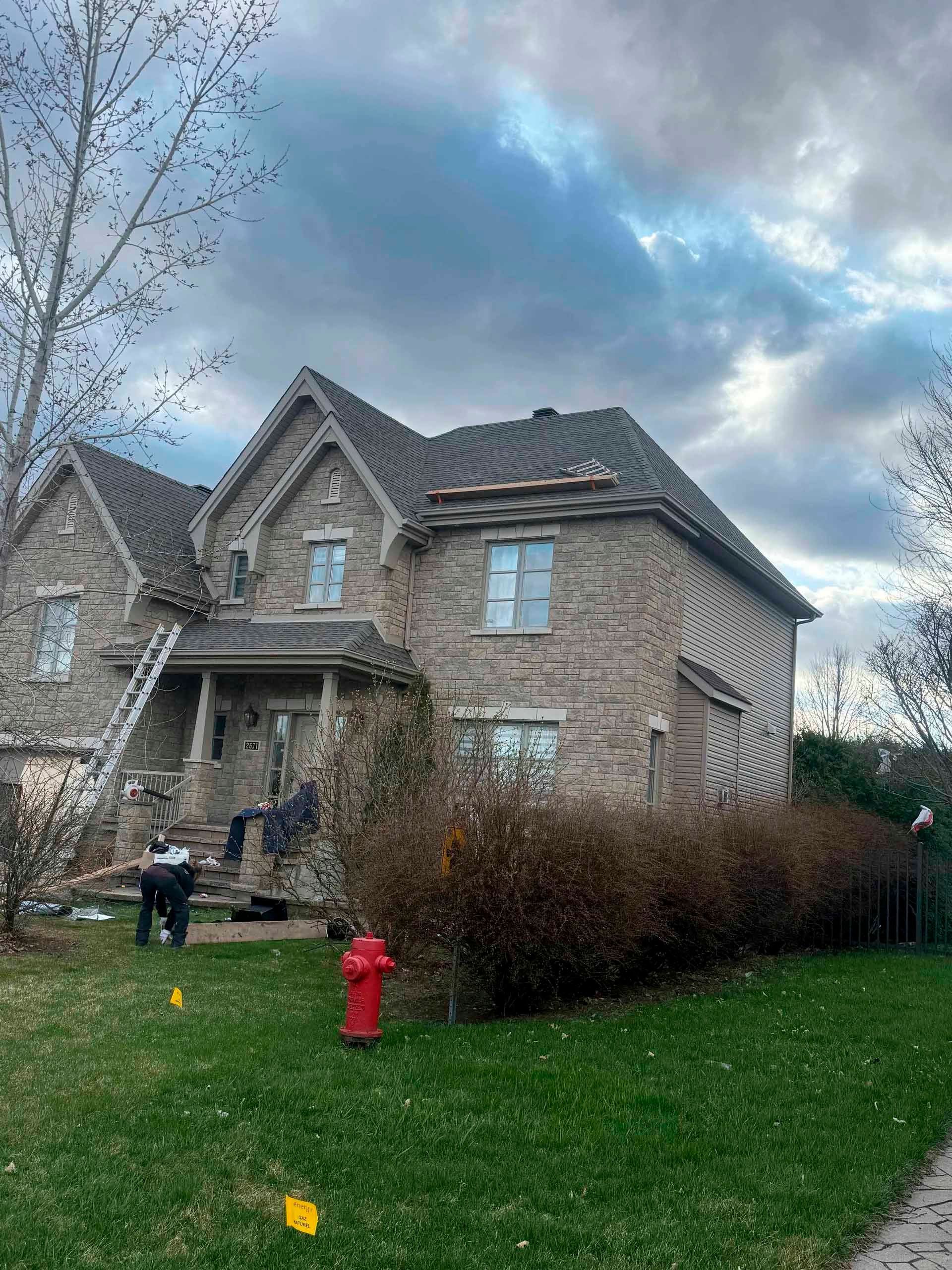 Maison en pierre à deux étages avec toit sombre. Des personnes et une échelle sur le côté. Ciel nuageux.