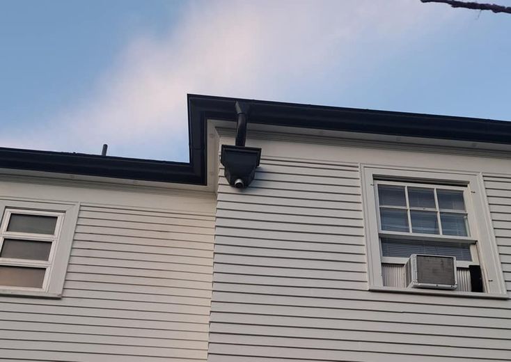 A white house with two windows and a black gutter