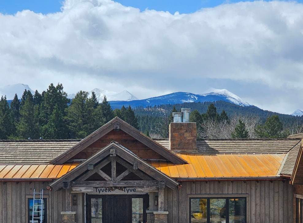 A large wooden house with a rusty roof and a mountain in the background.