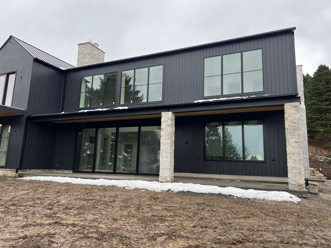A large black house with a lot of windows is sitting on top of a hill.