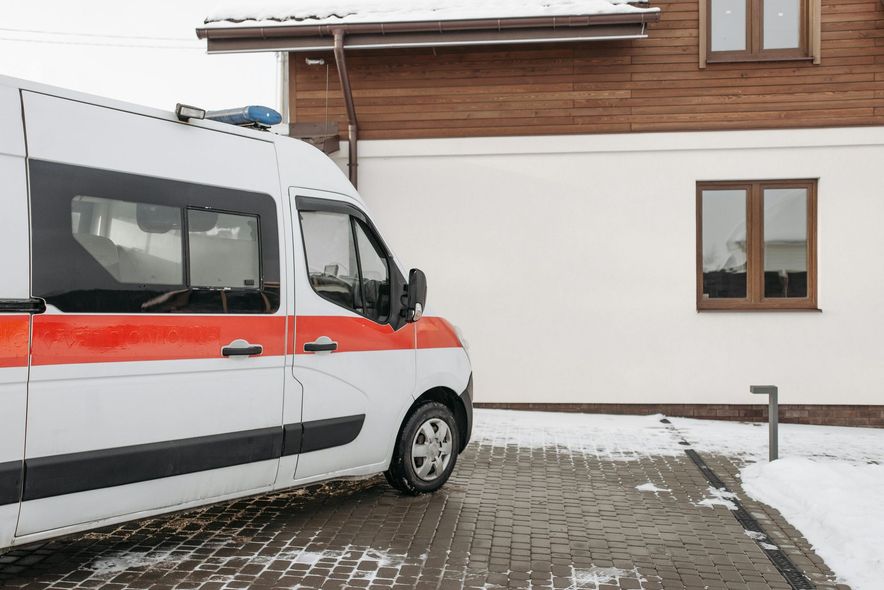 An ambulance is parked in front of a house in the snow.