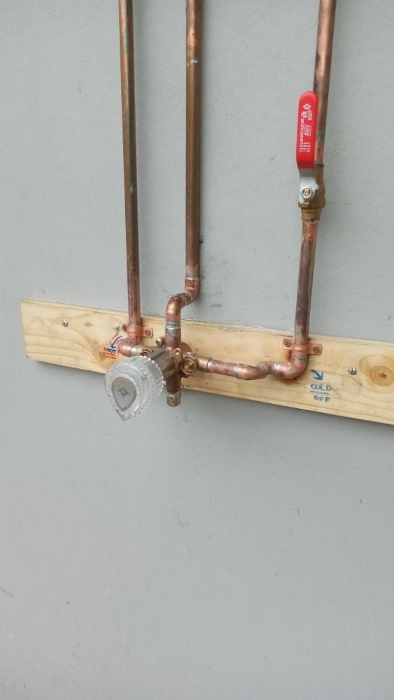 Copper pipes and valve attached to wooden board on gray wall.