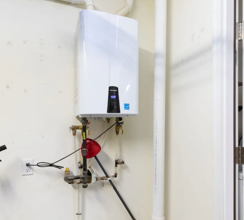 White wall-mounted tankless water heater with copper pipes and black wiring.