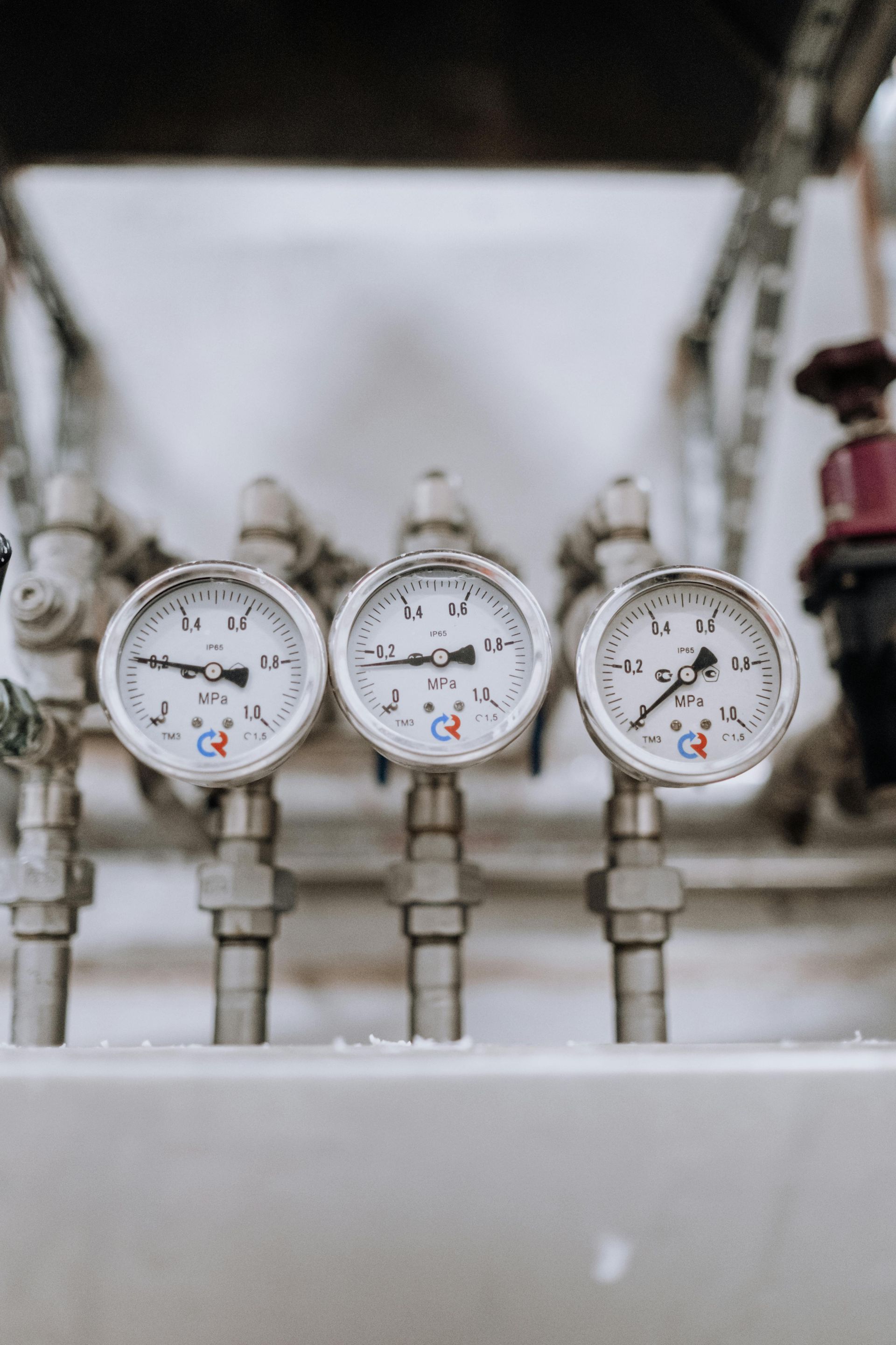 Three silver pressure gauges mounted on a white panel, showing different pressure levels.