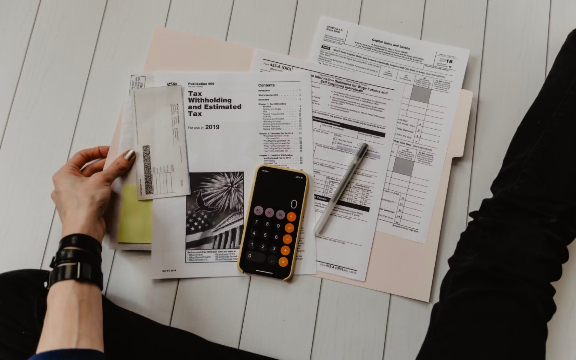 A person is sitting on the floor looking at papers and a cell phone.