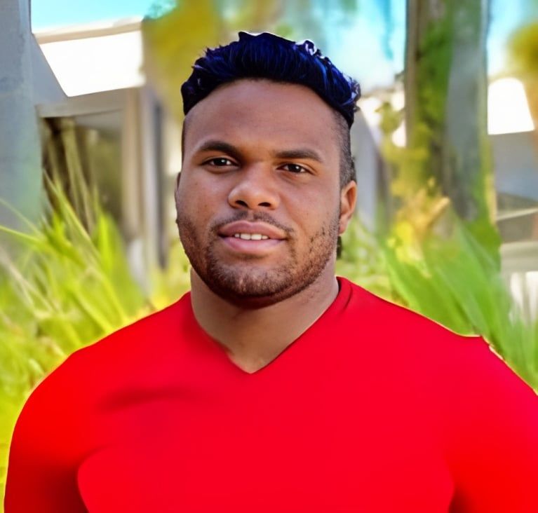 A man with a beard is wearing a red shirt and smiling for the camera.