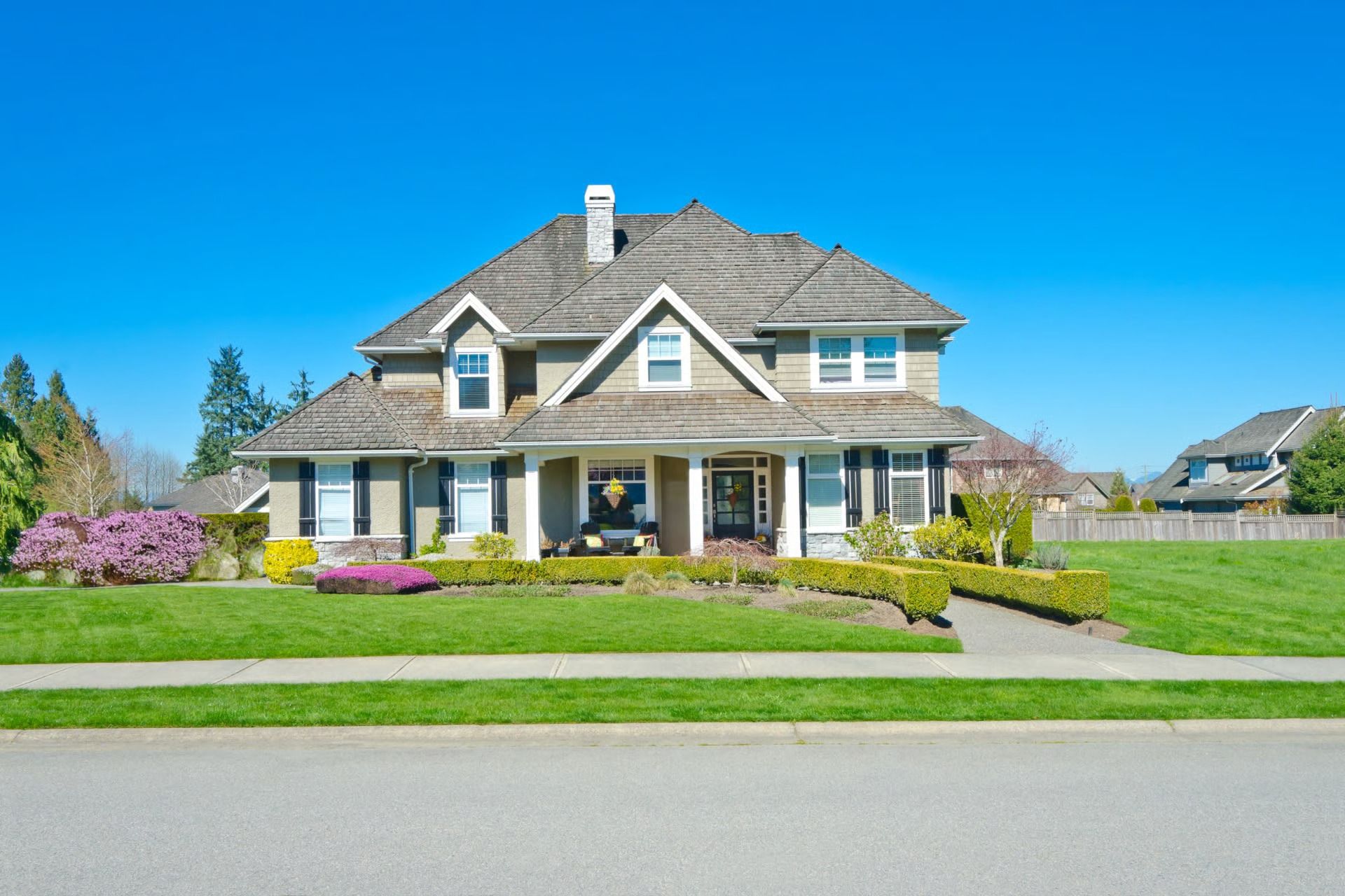 Large suburban house with a stone porch, manicured lawn, and bright blue sky