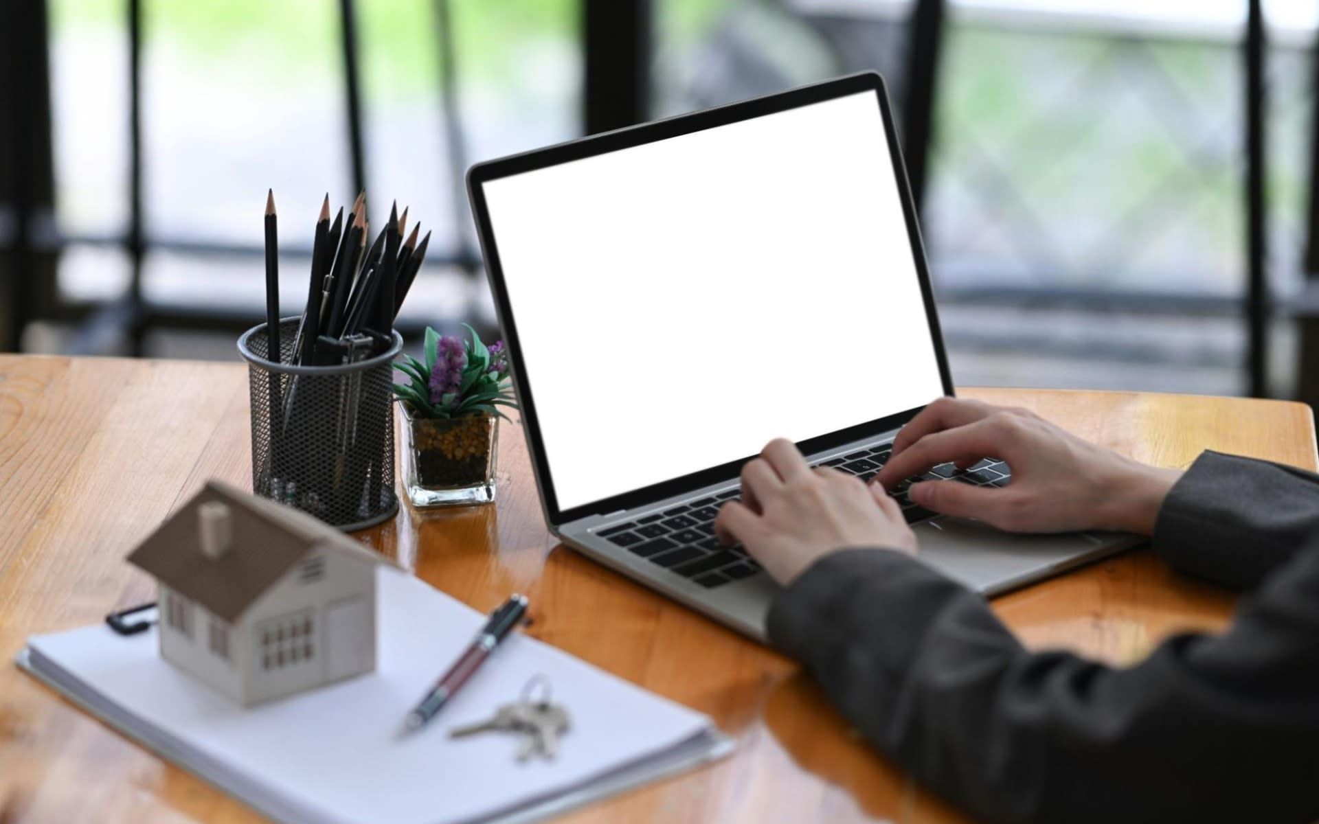 A person is typing on a laptop computer with a white screen.