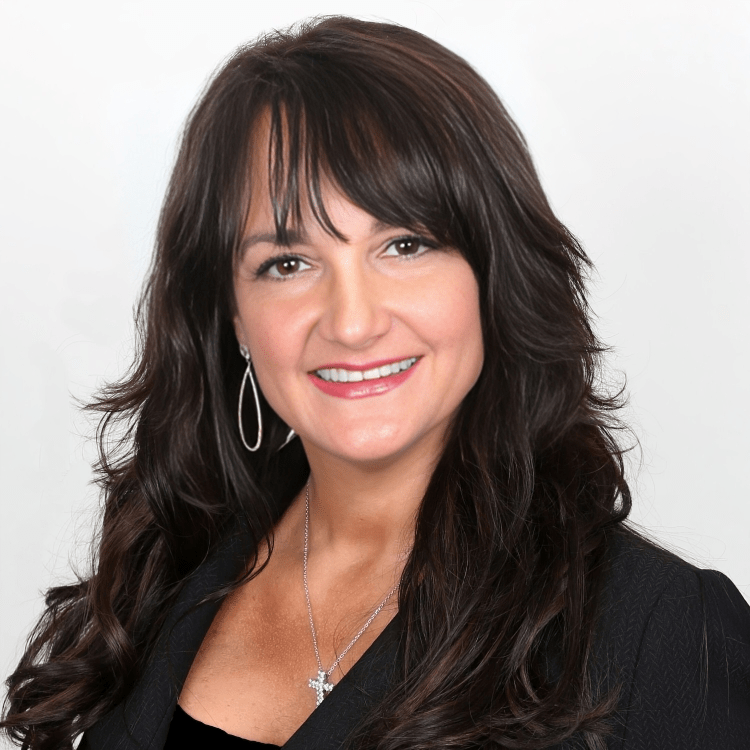 A woman wearing a black jacket and a cross necklace smiles for the camera