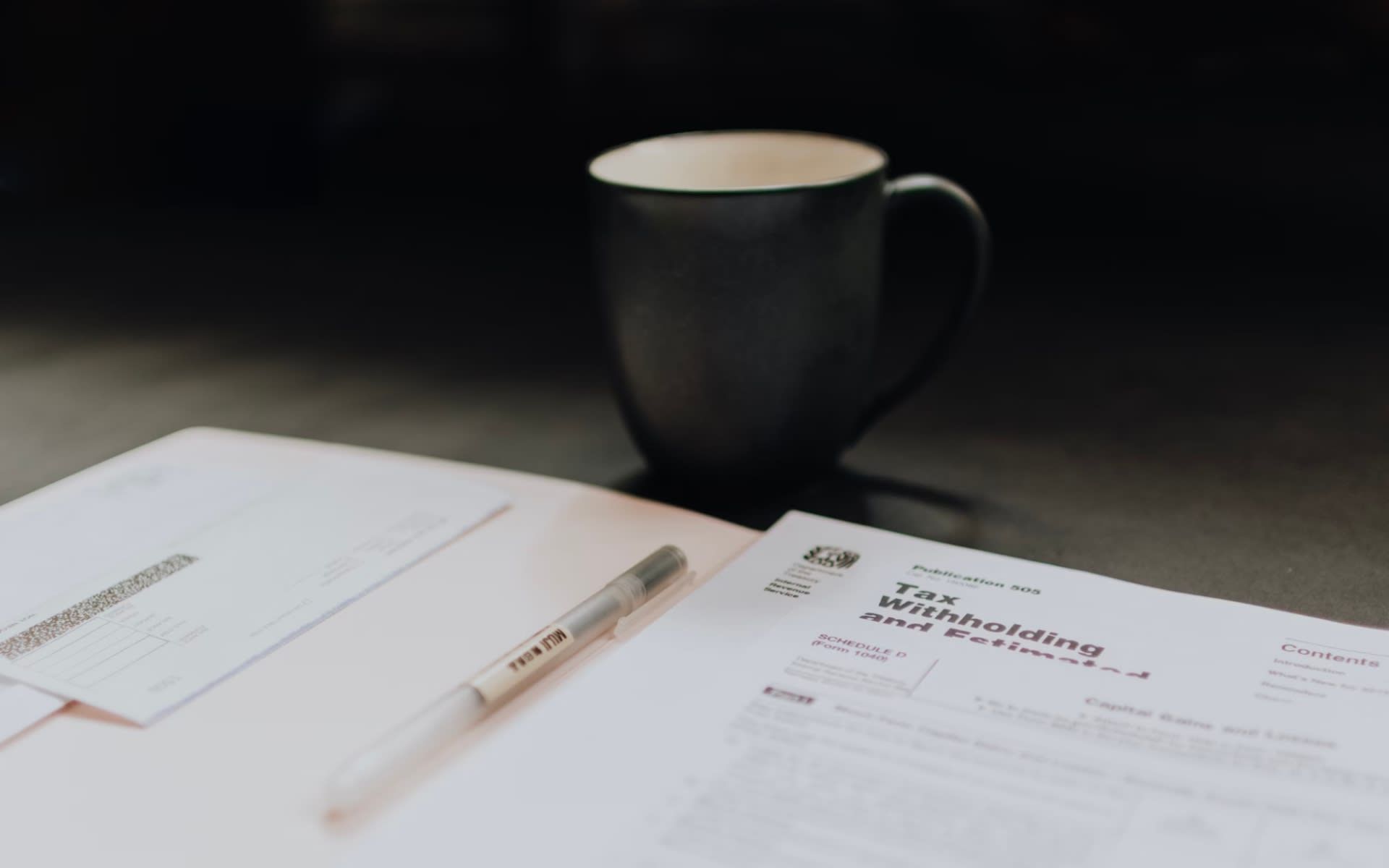 A cup of coffee is sitting on top of a piece of paper next to a pen.