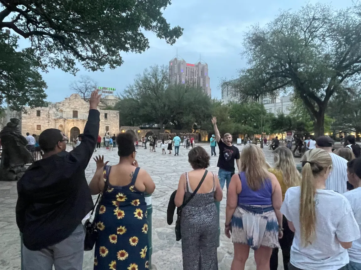 A group of people are standing in a park with their hands in the air.