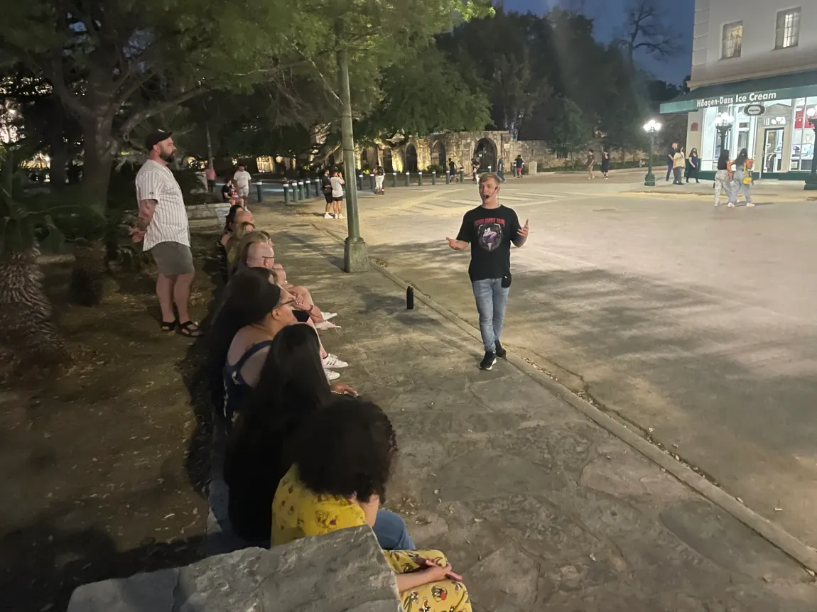 A group of people are standing on a sidewalk in a park at night.