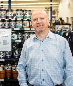 Man smiles, stands in store aisle in front of Yeti products, wearing a blue plaid shirt.