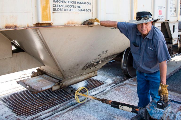 Man by a railcar, holding a tool, likely inspecting it for damage.