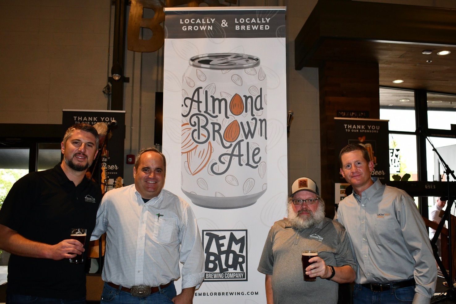 Four men stand in front of a banner for Almond Brown Ale.